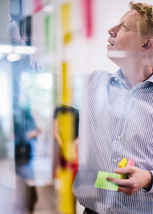 Mann steht vor einer transparenten Tafel mit Post-Its