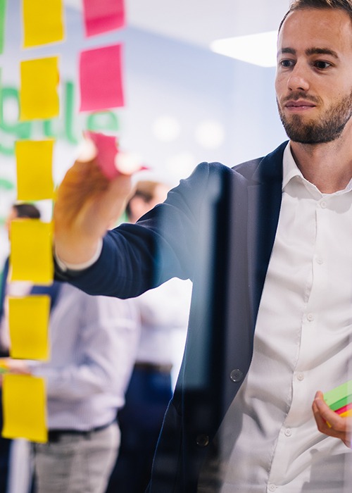 Mann steht vor einer transparenten Tafel mit Post-Its