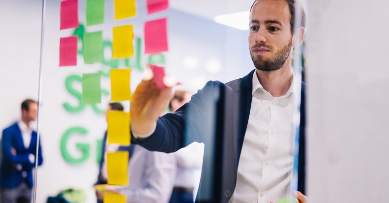 Mann steht vor einer transparenten Tafel mit Post-Its